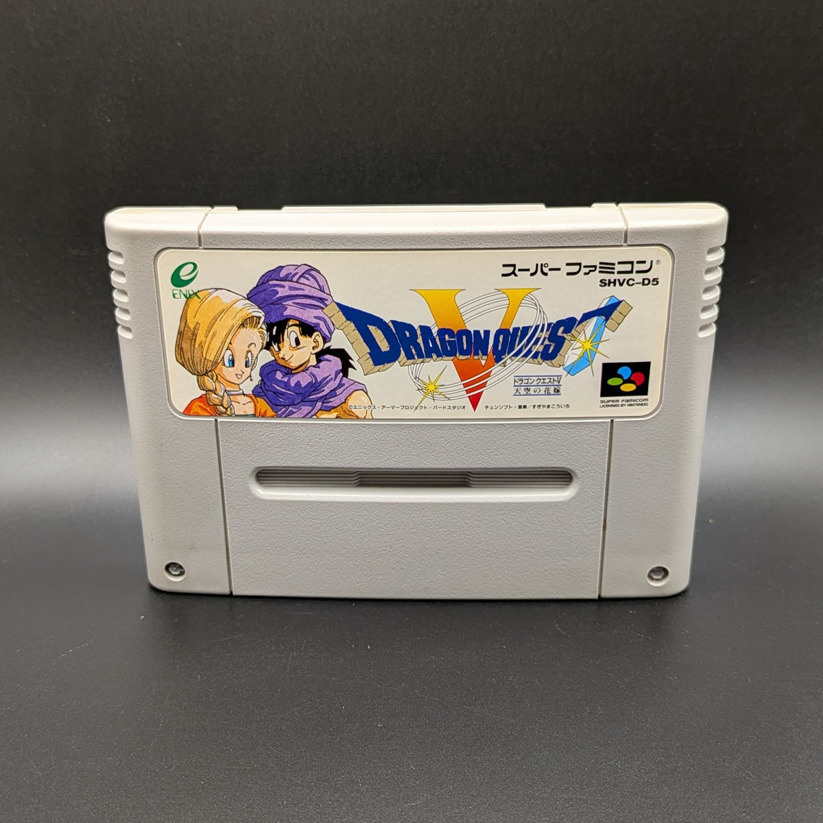 Dragon Quest V video game cartridge for Nintendo's Super Famicom (SFC) Entertainment System, shown standing up and facing forwards on a dark grey background.