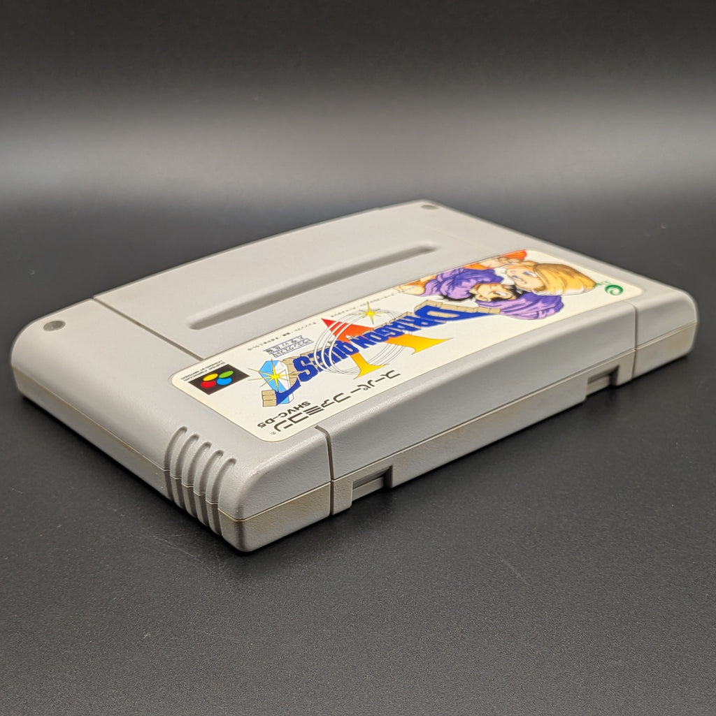 Dragon Quest V video game cartridge for Nintendo's Super Famicom (SFC) Entertainment System, shown laying on its back with the label facing upwards. Showing the right hand side and top edge. It sits on a dark grey background.