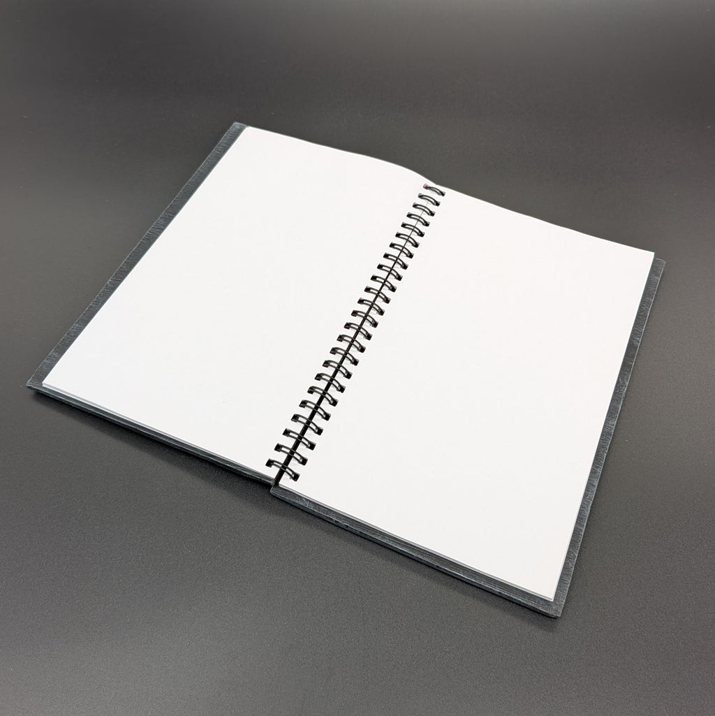 An open spiral-bound notebook with blank white pages, resting on a dark gray surface.