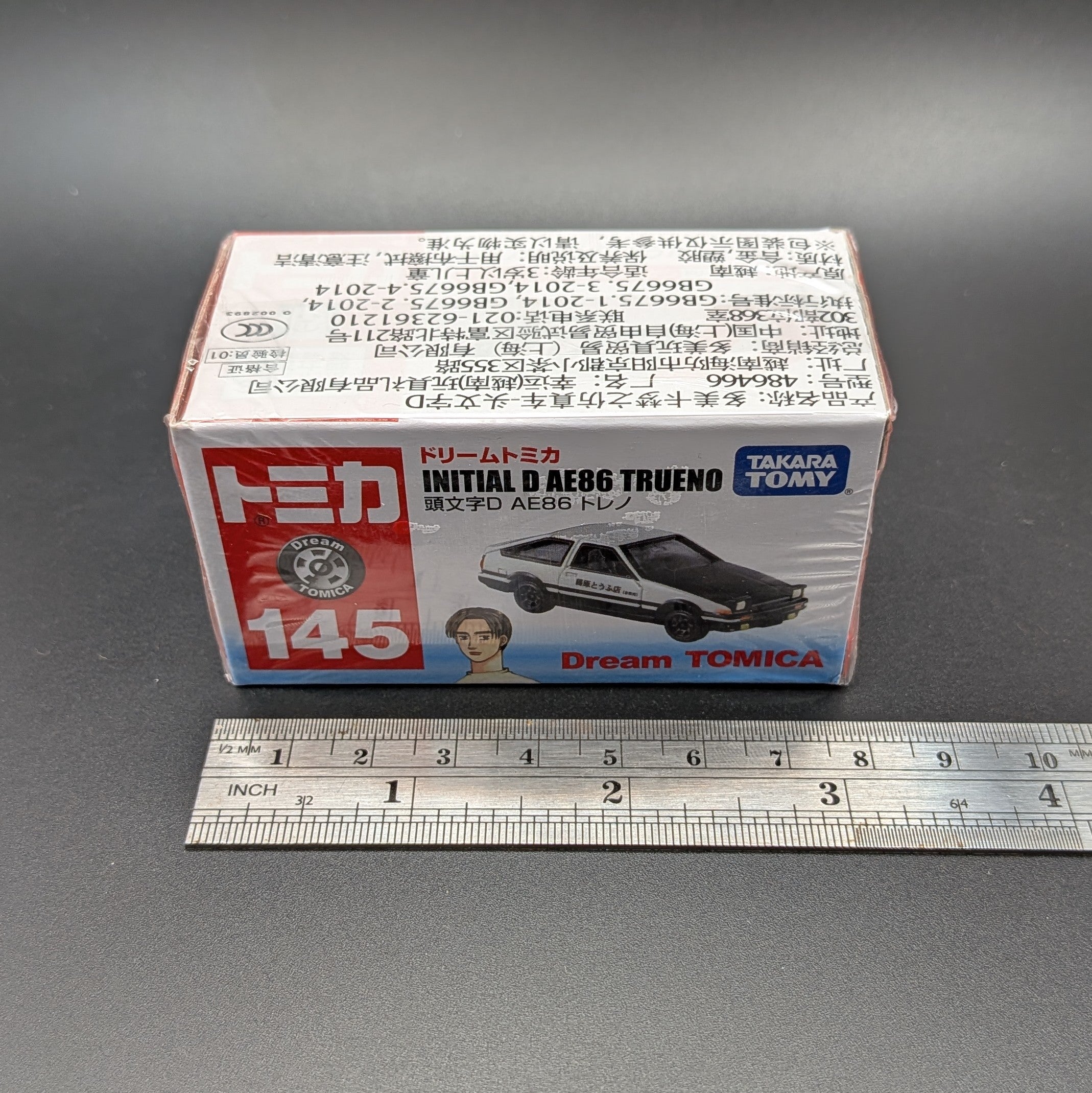 DreamTomica #145 AE86 Trueno from Intial D. Box facing forwards straight on, with a metal ruler, on a grey background.