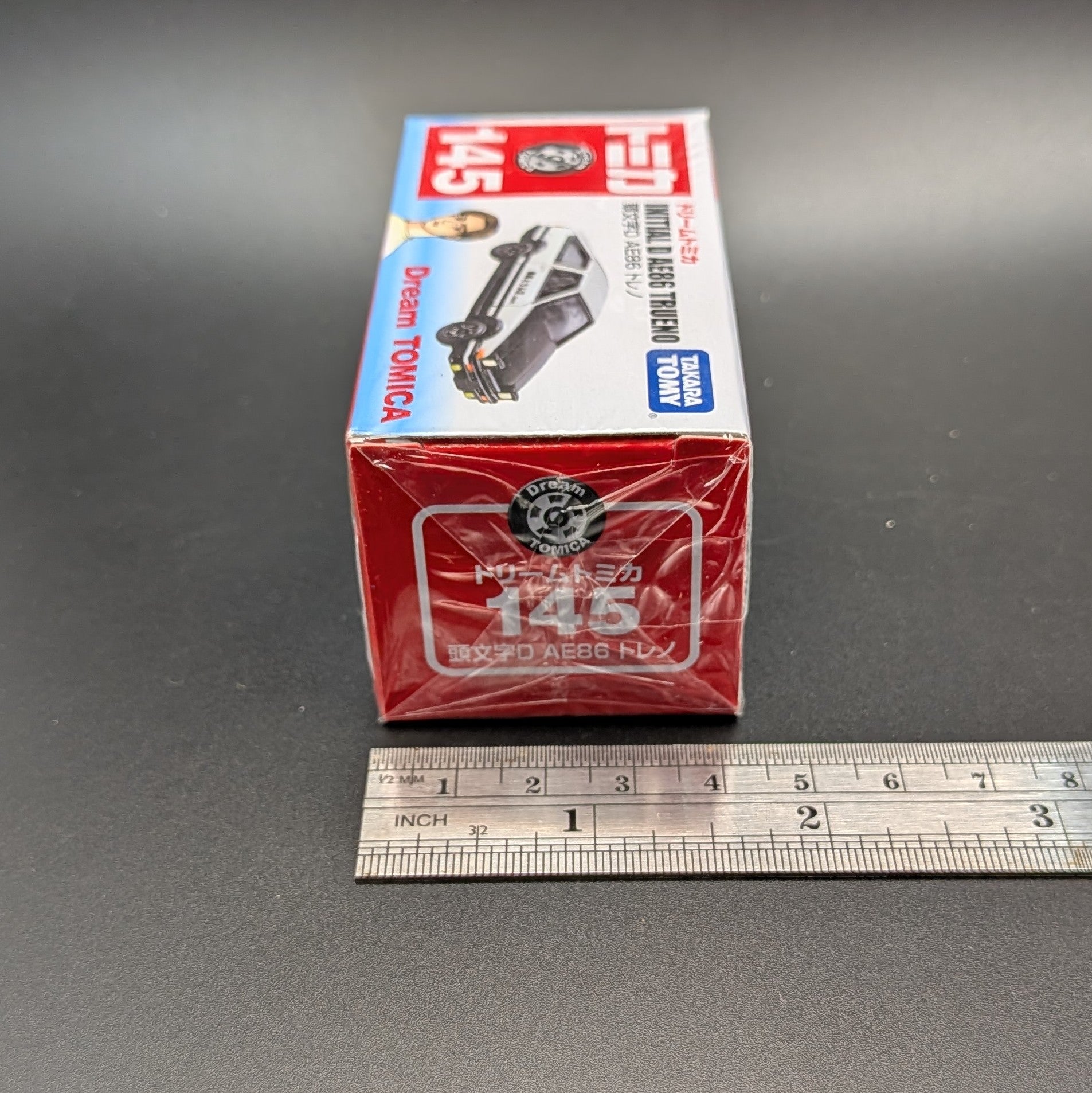 DreamTomica #145 AE86 Trueno from Intial D. Box facing side on with a metal ruler, on a grey background.