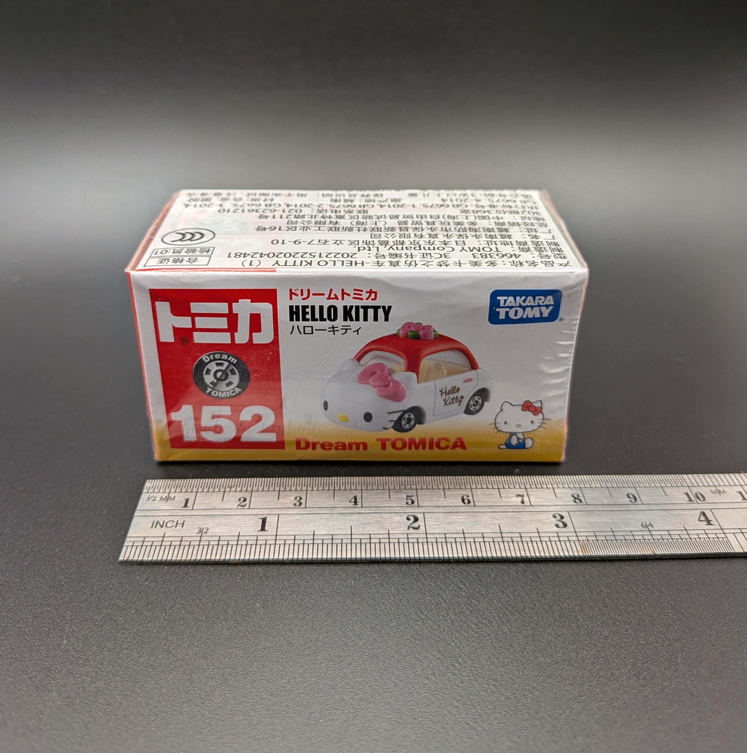 Model car packaging with 'Hello Kitty' design on a gray background, featuring a ruler for scale.