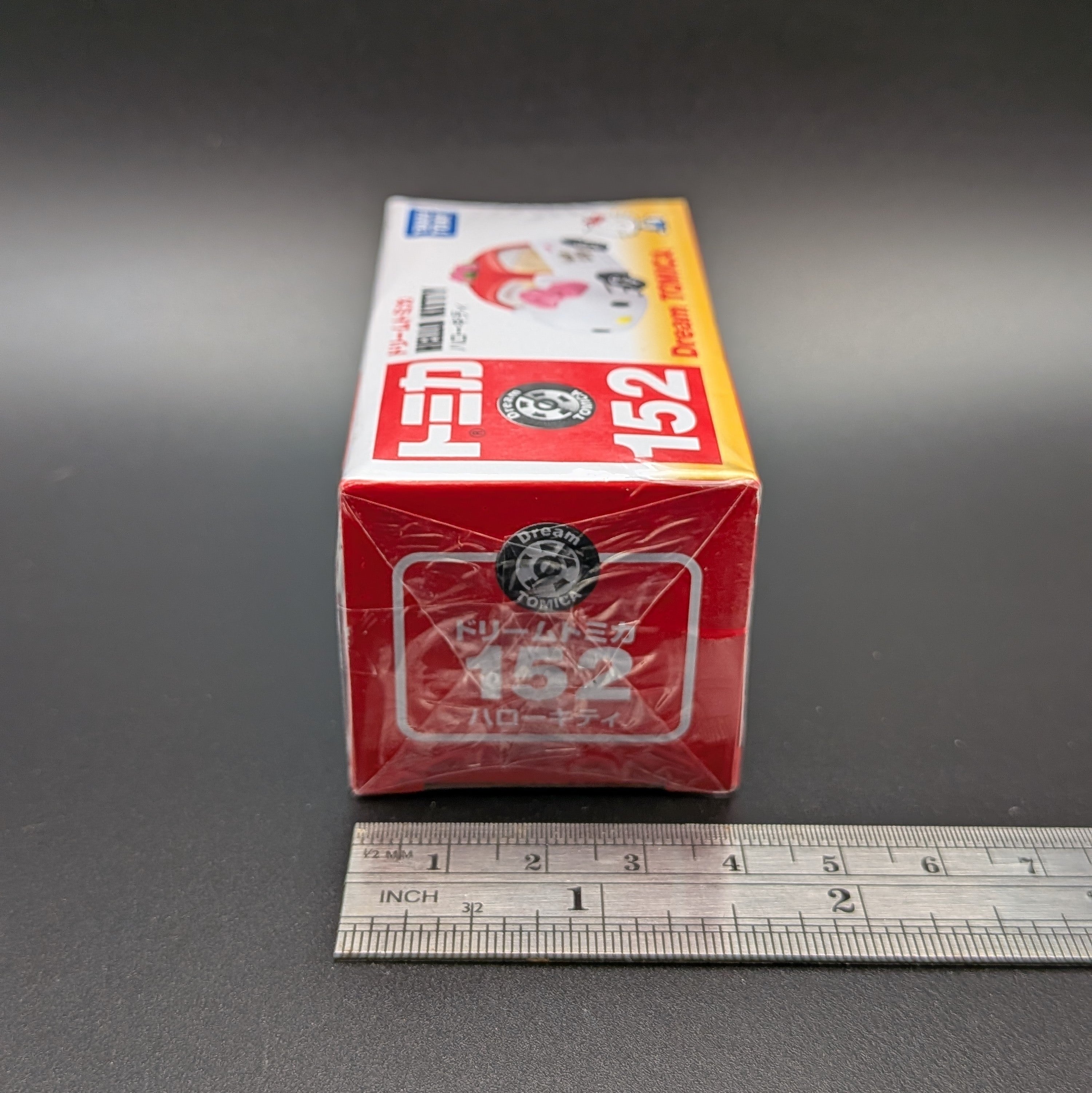 Dream Tomica Red and white box with '152' on a gray background, next to a ruler for scale.