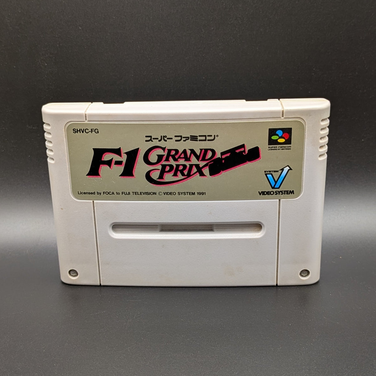 F-1 Grand Prix video game cartridge for Nintendo's Super Famicom (SFC) Entertainment System, shown standing up and facing forwards on a dark grey background.
