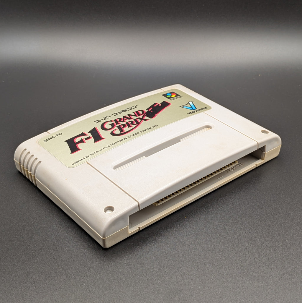 F-1 Grand Prix video game cartridge for Nintendo's Super Famicom (SFC) Entertainment System, shown laying on its back with the label facing upwards. Showing the left hand side and bottom slot. It sits on a dark grey background