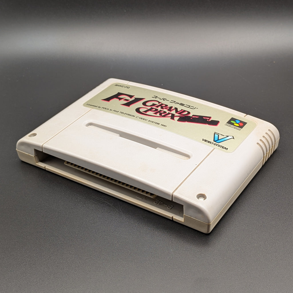 F-1 Grand Prix video game cartridge for Nintendo's Super Famicom (SFC) Entertainment System, shown laying on its back with the label facing upwards. Showing the right hand side and bottom slot. It sits on a dark grey background