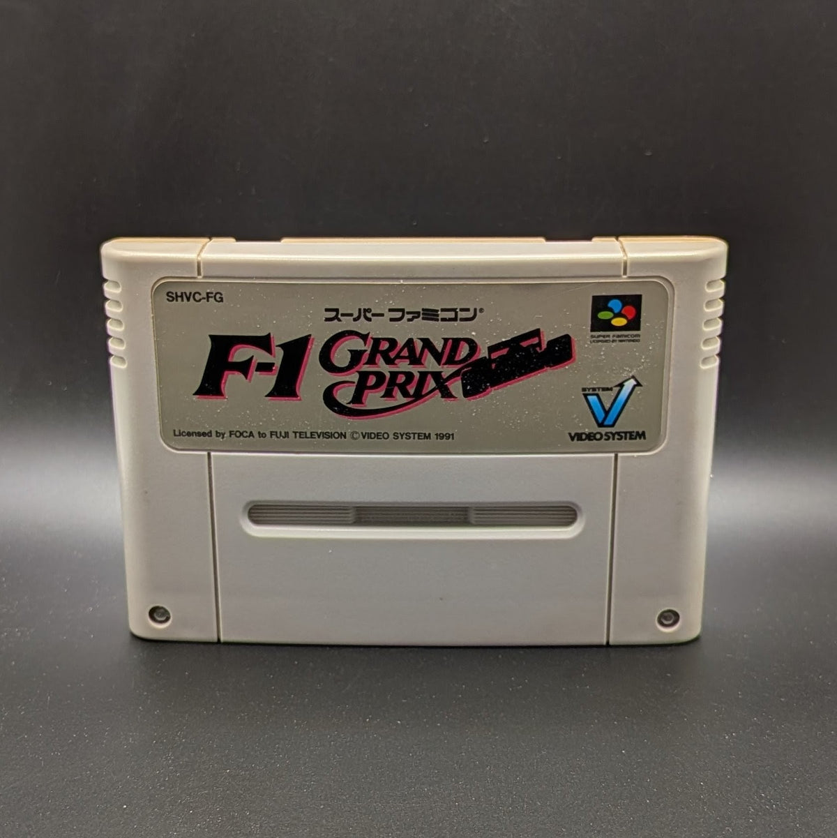 F-1 Grand Prix video game cartridge for Nintendo's Super Famicom (SFC) Entertainment System, shown standing up and facing forward on a dark grey background.
