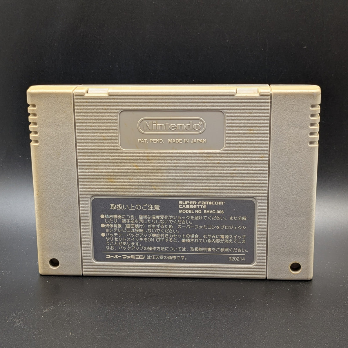 F-1 Grand Prix video game cartridge for Nintendo's Super Famicom (SFC) Entertainment System, shown from the back, standing up on a dark grey background. You can see yellowing on the back panel.