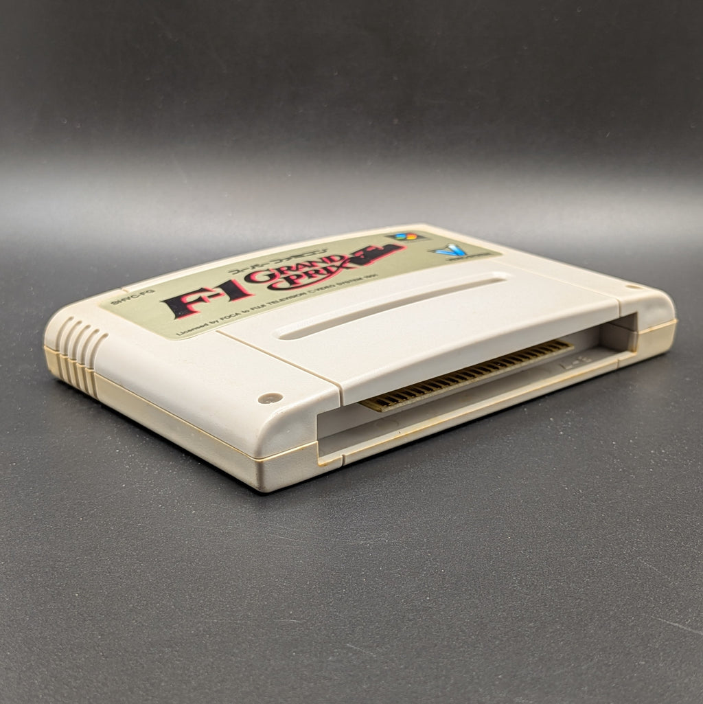 F-1 Grand Prix video game cartridge for Nintendo's Super Famicom (SFC) Entertainment System, shown laying on its back with the beige label facing up on a dark grey background.
