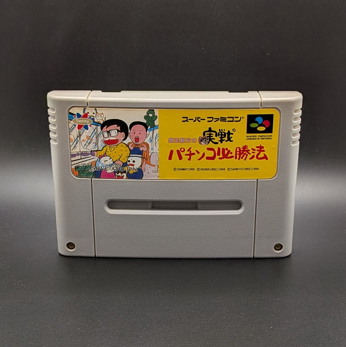 Gindama Oyakata no Jissen Pachinko video game cartridge for Nintendo's Super Famicom (SFC) Entertainment System, shown standing up and facing forward on a dark grey background.
