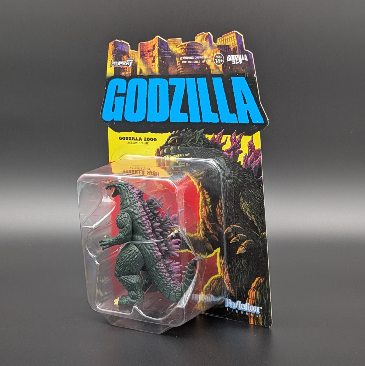Godzilla 2000 action figure in its original blister packaging, featuring a dark green Godzilla figure with purple spines against a yellow and red illustrated backing card with a large blue GODZILLA logo.