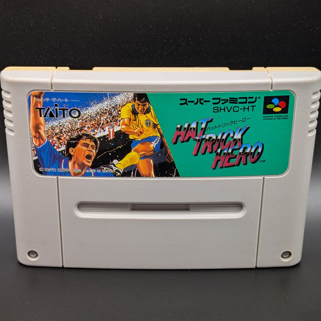 A close up of Hat Trick Hero video game cartridge for Nintendo's Super Famicom (SFC) Entertainment System, shown standing up and facing forwards on a dark grey background.