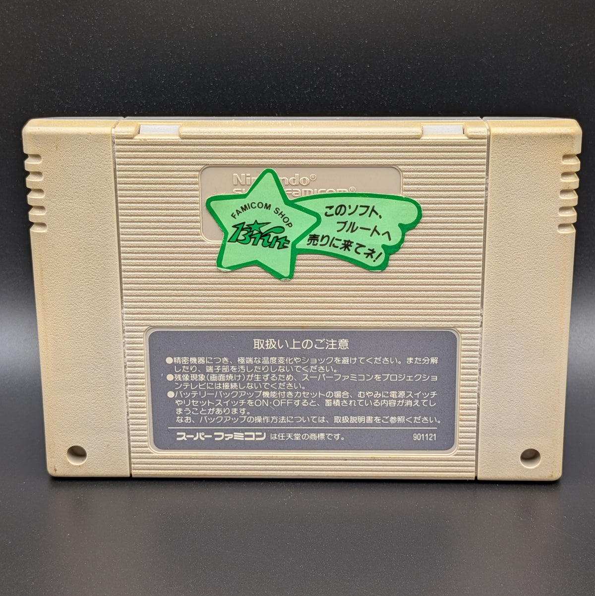 Hat Trick Hero video game cartridge for Nintendo's Super Famicom (SFC) Entertainment System, showing the back of the cartridge. It sits on a dark grey background. It has a green star label attached to the back with Japanese writing.