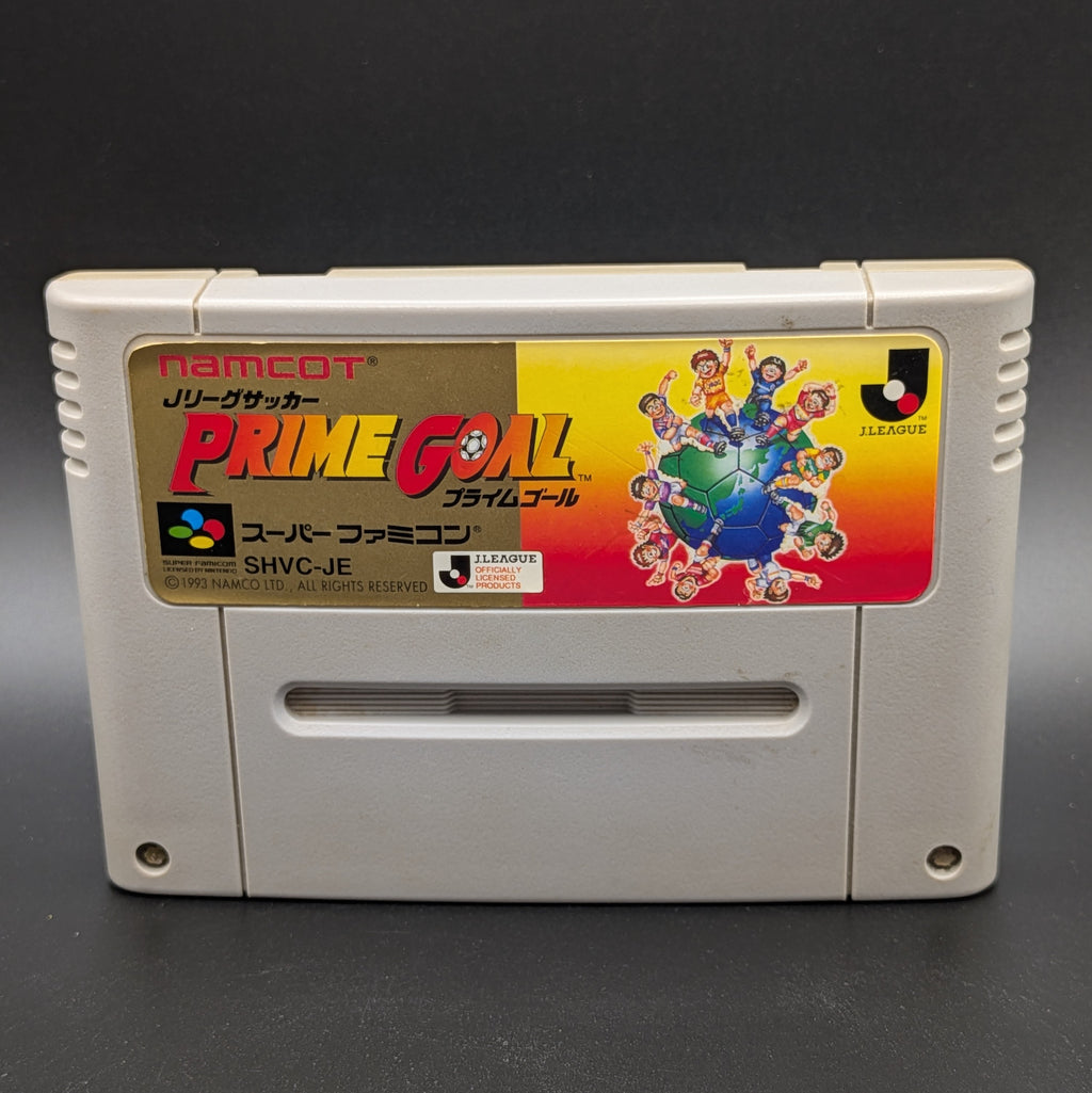 A close up of J-League Soccer Prime Goal video game cartridge for Nintendo's Super Famicom (SFC) Entertainment System, shown standing up and facing forwards on a dark grey background.