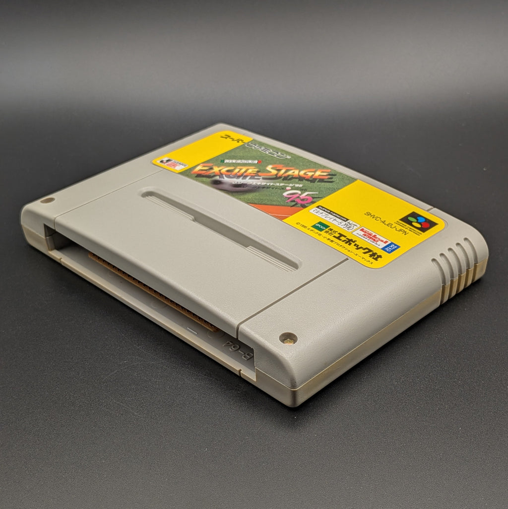 J-League Excite Stage '95 video game cartridge for Nintendo's Super Famicom (SFC) Entertainment System, shown laying on its back with the label facing upwards. Showing the right hand side and bottom slot. It sits on a dark grey background.