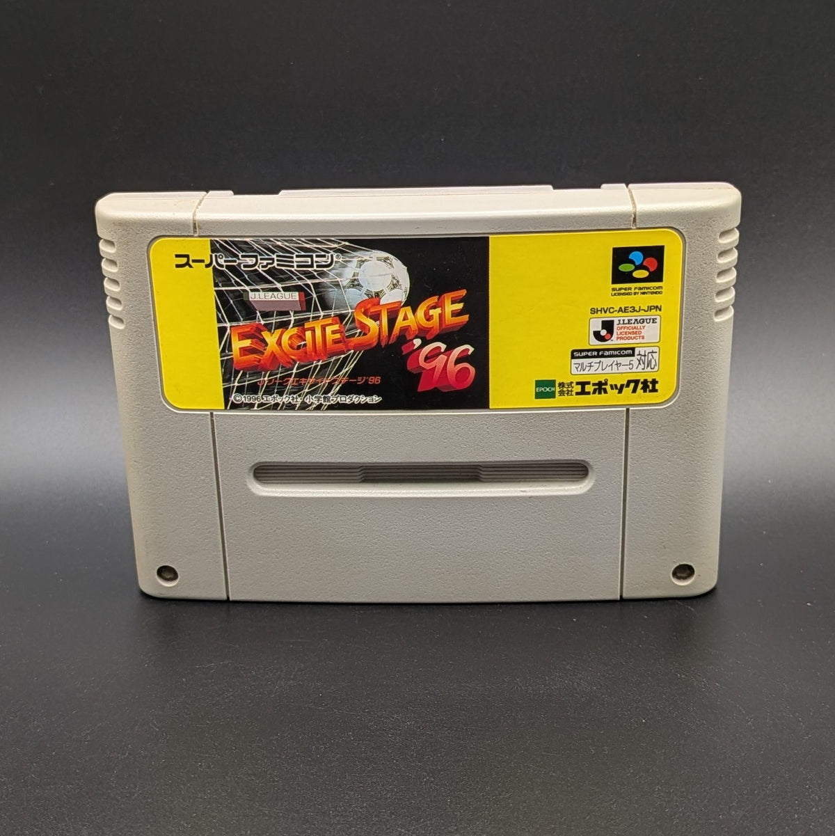 J League Excite Stage '96 video game cartridge for Nintendo's Super Famicom (SFC) Entertainment System, shown standing up and facing forward on a dark grey background.