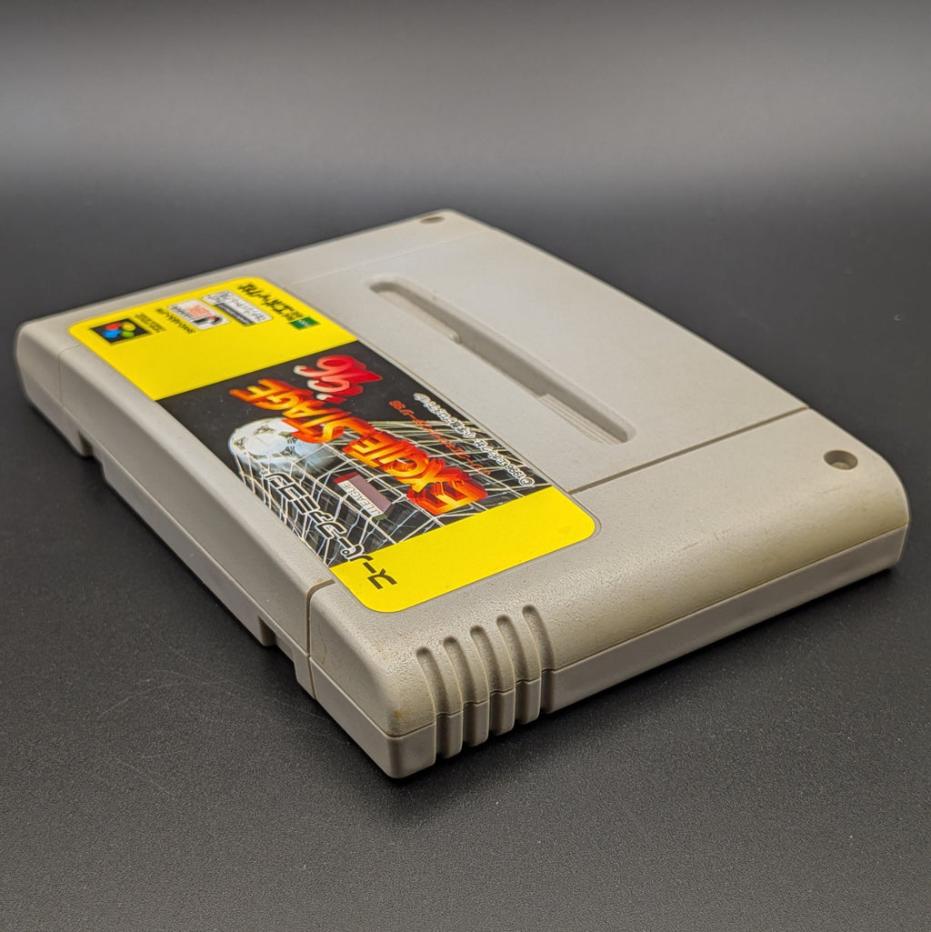 J League Excite Stage '96 video game cartridge for Nintendo's Super Famicom (SFC) Entertainment System, shown laying on its back with the label facing upwards. Showing the left hand side and top edge. The cart is displayed on a dark grey background