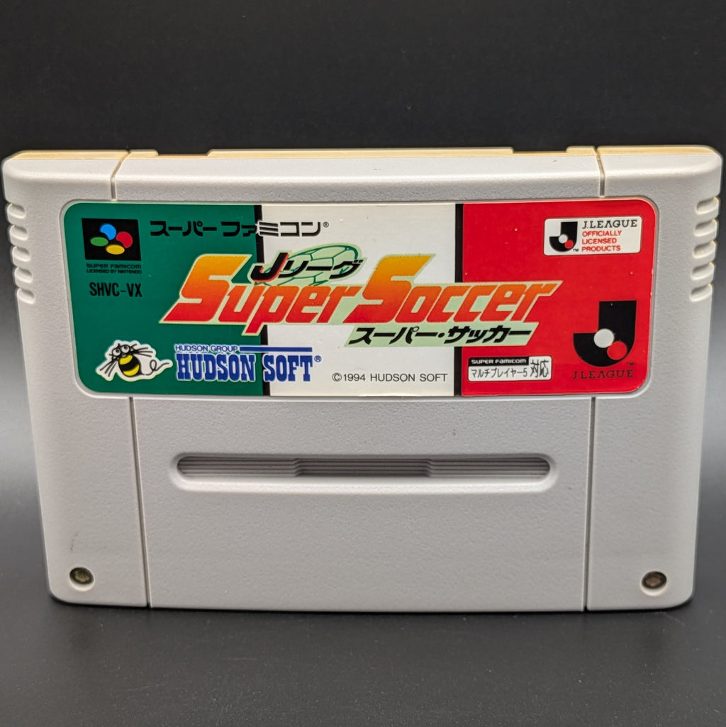 A close up of J League Super Soccer video game cartridge for Nintendo's Super Famicom (SFC) Entertainment System, shown standing up and facing forwards on a dark grey background.