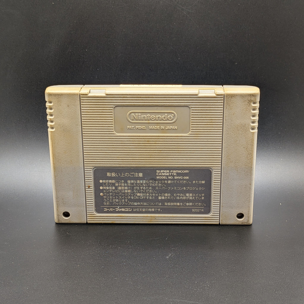 J League Super Soccer video game cartridge for Nintendo's Super Famicom (SFC) Entertainment System, shown from the back, standing up on a dark grey background. You can see yellowing on the back panel and a hand-written Japanese sticker on the top edge.