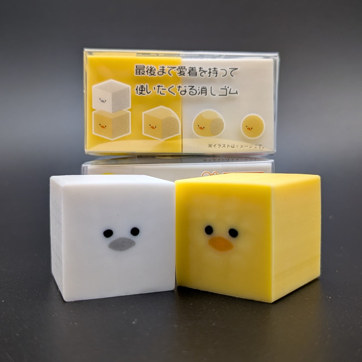 Two small square character-shaped erasers sitting next to each other, one white duck and one yellow. The side of the package can be seen in the background, showing an image guide of how the eraser works and changes shape over time.