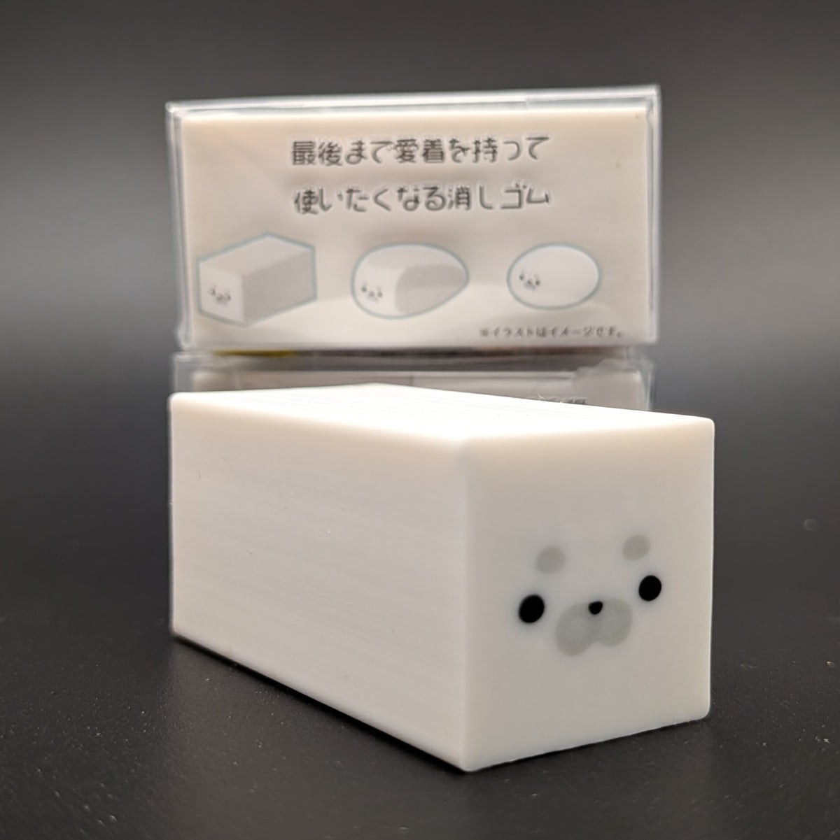 A small white rectangular character-shaped eraser with a cute seal face on the end. The side of the package can be seen in the background, showing an image guide of how the eraser works and changes shape over time.