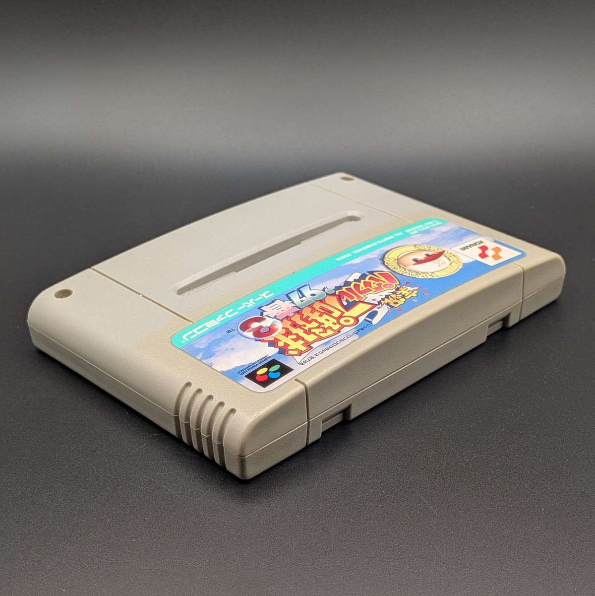 Jikkyou Powerful Pro Yakyuu 3 '97 video game cartridge for Nintendo's Super Famicom (SFC) Entertainment System, shown laying on its back with the label facing upwards. Showing the right hand side and top edge. It sits on a dark grey background