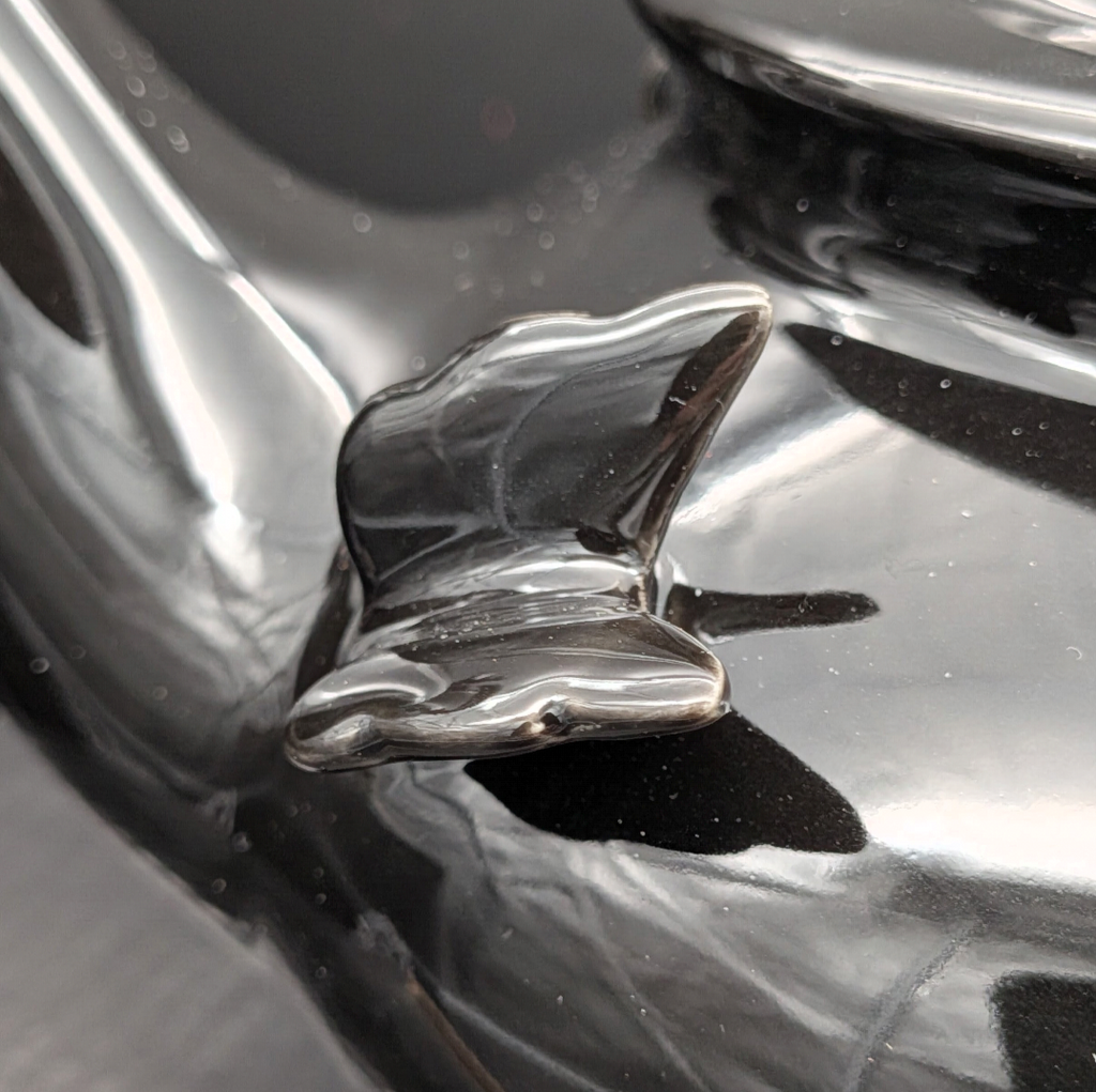 A close-up of a glossy black sculpted butterfly ceramic detail off the side of the teapot.