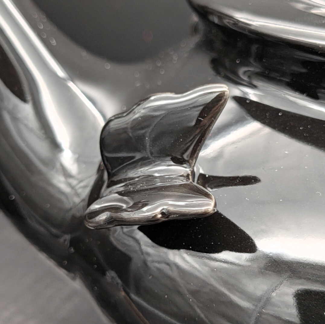 A close-up of a glossy black sculpted butterfly ceramic detail off the side of the teapot.