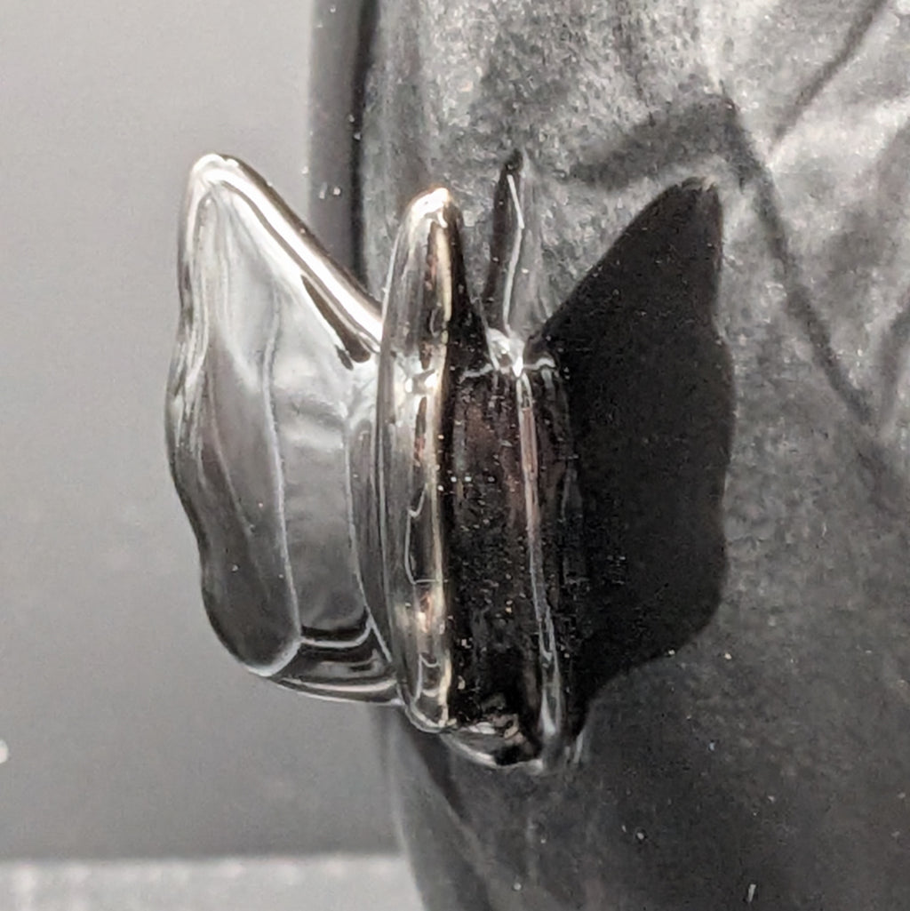 A close-up of a glossy, sculptured black butterfly detail on the side of the jar.