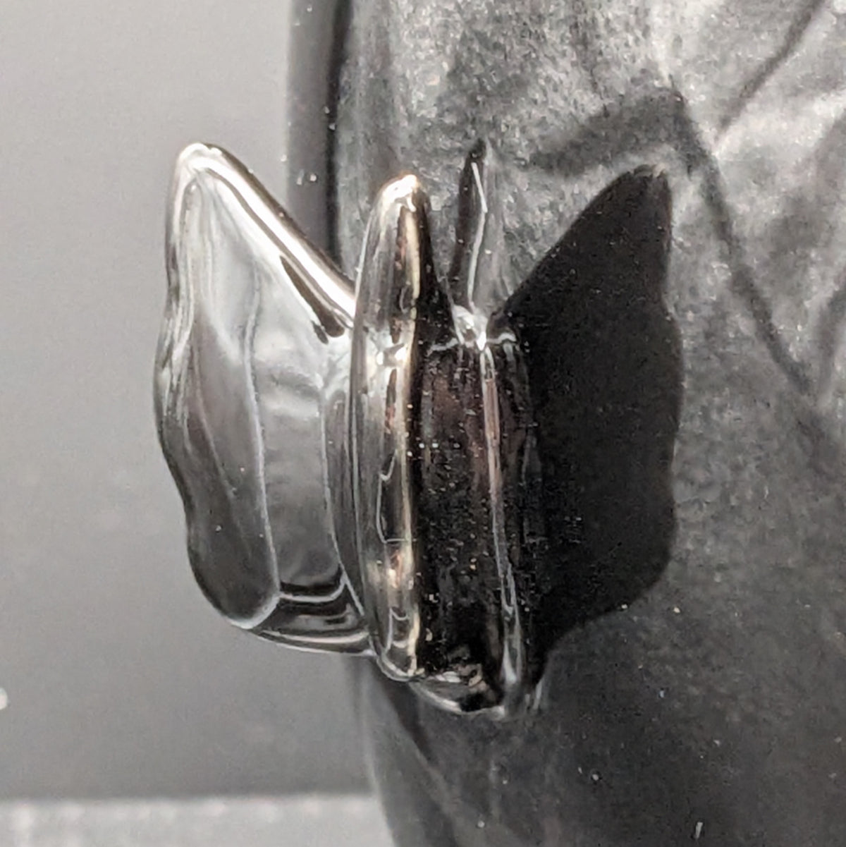 A close-up of a glossy, sculptured black butterfly detail on the side of the jar.