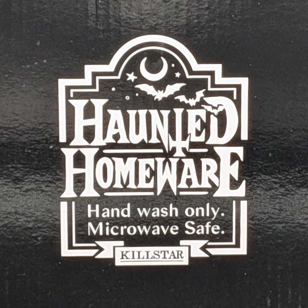 A white decorative label with the words 'HAUNTED HOMEWARE' and smaller text 'Hand wash only. Microwave Safe.