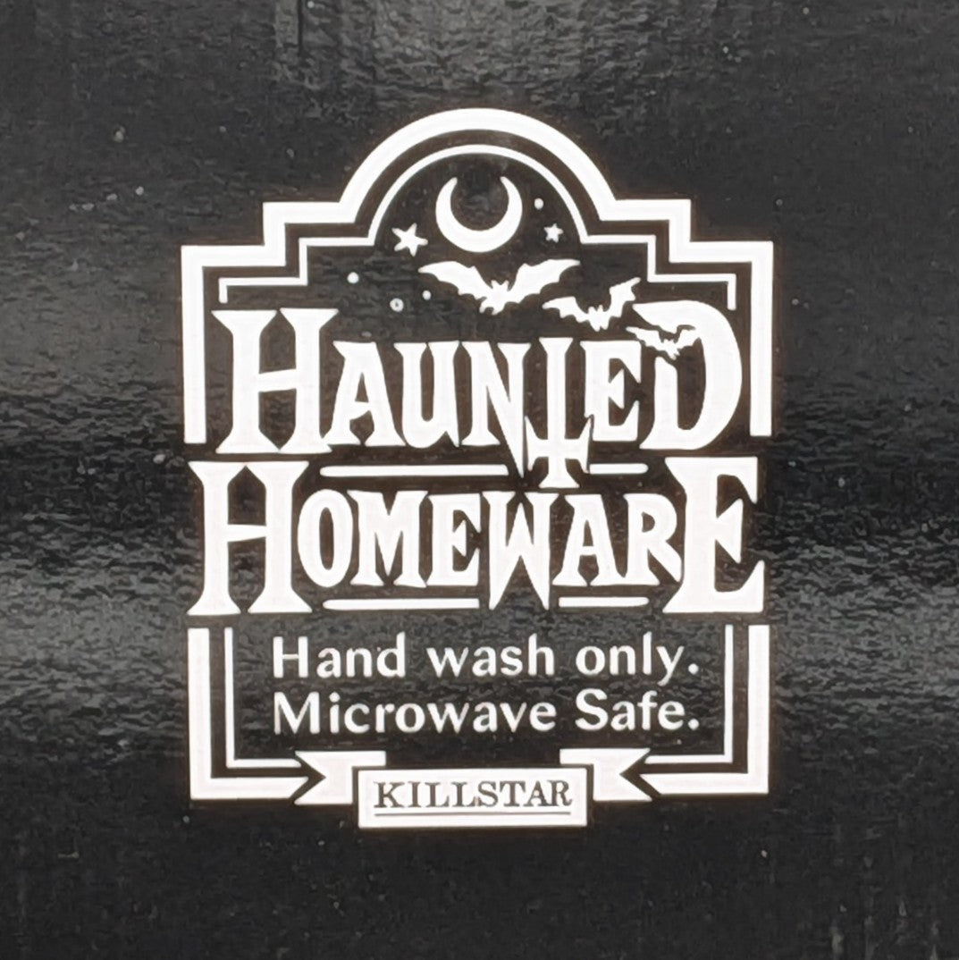 A white decorative label with the words 'HAUNTED HOMEWARE' and smaller text 'Hand wash only. Microwave Safe.