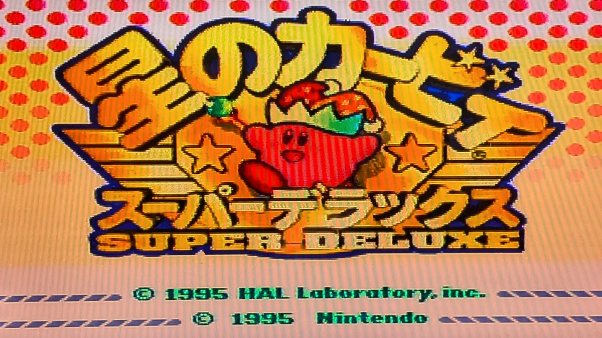 The digital game title screen for Kirby's Dream Land Super Deluxe for Nintendo's Super Famicom (SFC), featuring a large logo with large stylized Japanese text, Kirby with a jester hat and staff in the center on an orange background, and copyright text for HAL Laboratory and Nintendo at the bottom. This shows the game tested and working.