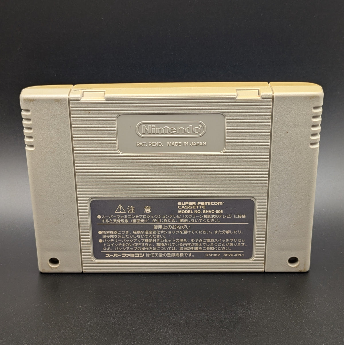 Kirby's Dream Land Super Deluxe video game cartridge for Nintendo's Super Famicom (SFC) Entertainment System, showing the back of the cartridge, you can see yellowing across the top edge. Displayed a dark grey background.