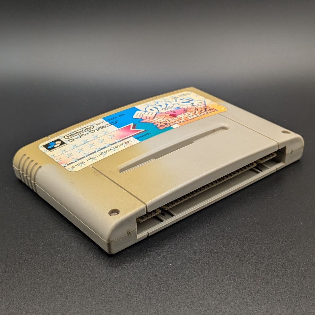 Kirby's Dream Land Super Deluxe video game cartridge for Nintendo's Super Famicom (SFC) Entertainment System, shown laying on its back with the label facing upwards. Showing the left hand side and bottom slot. It has large areas of yellowing and the label has faded. Displayed a dark grey background.