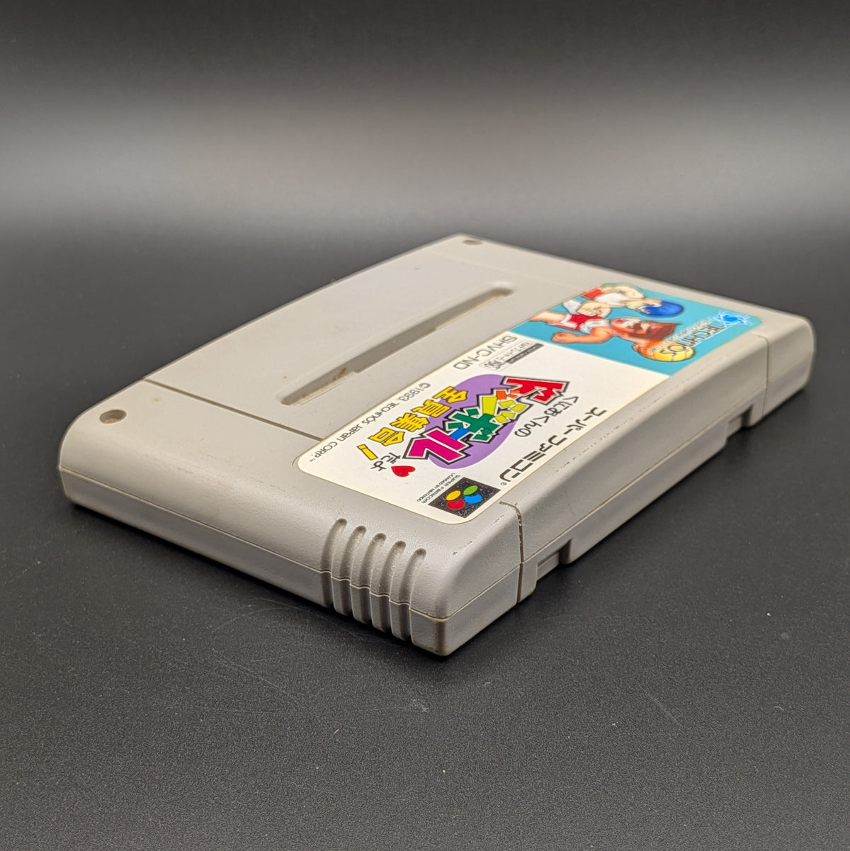 Kunio-Kun no Dodgeball video game cartridge for Nintendo's Super Famicom (SFC) Entertainment System, shown laying on its back with the label facing upwards. Showing the right hand side and top edge. It sits on a dark grey background