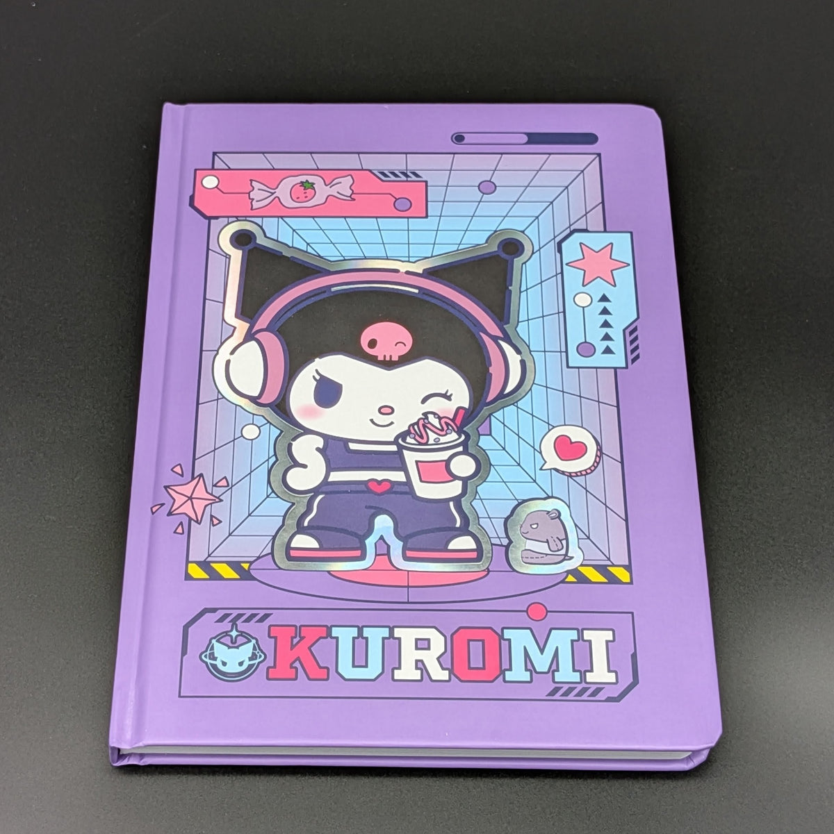 A purple Kuromi ruled notebook with a colourful cartoon cover illustration, photographed on a dark gray background. From the Sanrio POP range, printed by Blue Sky Studios.