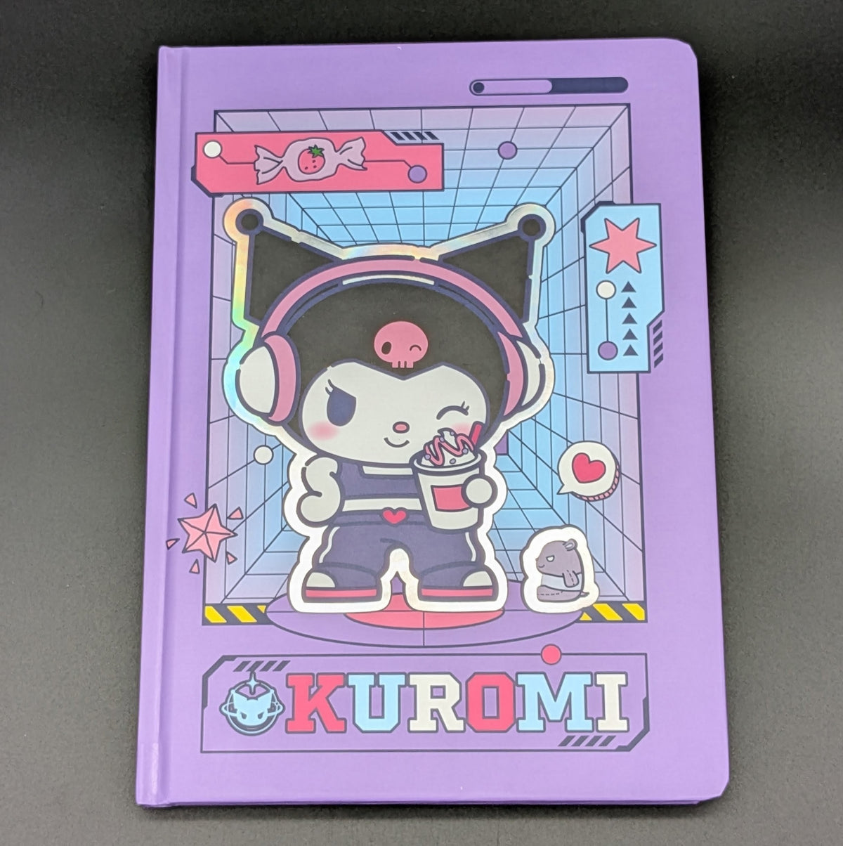 A purple Kuromi ruled notebook with a colourful cartoon cover illustration, shown face on, photographed on a dark gray background. From the Sanrio POP range, printed by Blue Sky Studios.