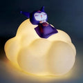 A cloud-shaped LED night light glowing with warm yellow light, featuring a small purple cartoon character figurine sitting on top against a dark background.
