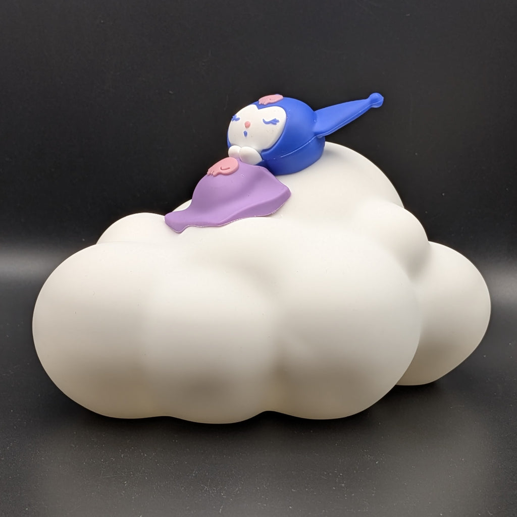 A Kuromi cloud-shaped collectible figure from Sanrio, featuring a white cloud base with a blue and purple Kuromi character sitting on top, set against a dark gray background.