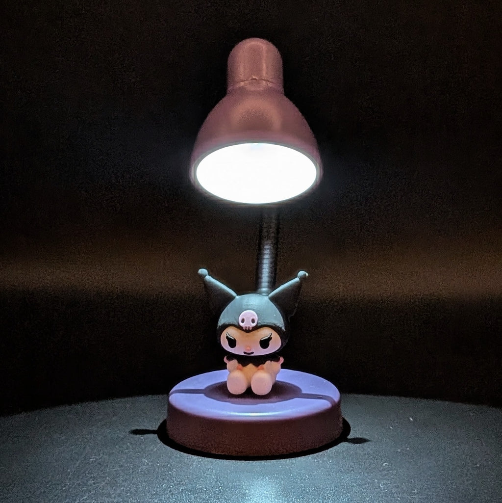 A small tabletop lamp with a cartoon character figure on the base, photographed in a dark setting. The lampshade glows white from an attached bulb.