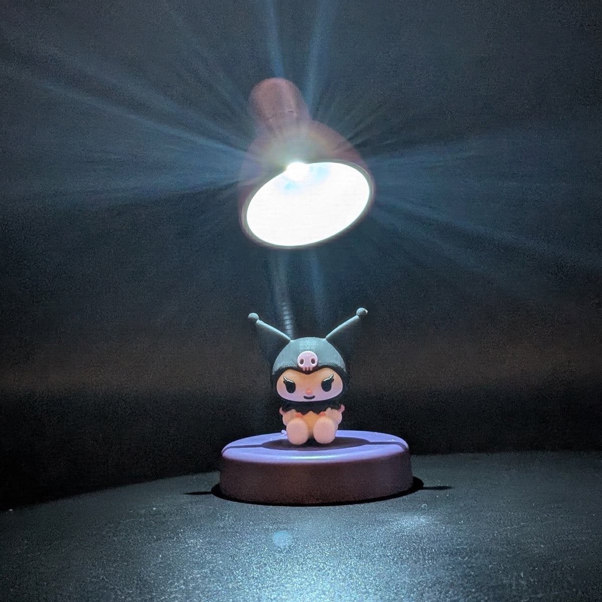 A small character figurine sits on a round base under a glowing lamp, with dramatic light rays shining down against a dark background.