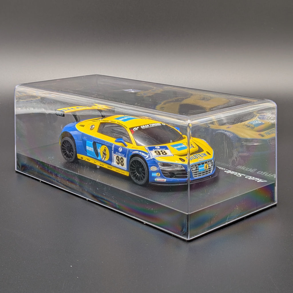 A yellow and blue scale model car displayed inside a clear plastic display case on a dark gray background.
