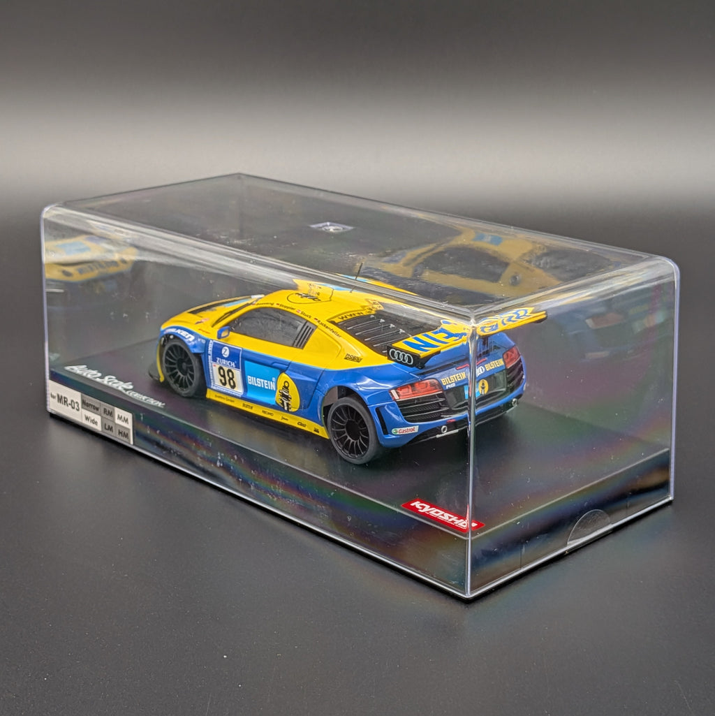 A diecast model race car in a clear display case on a dark gray background. The car is yellow and blue with racing decals, and the case has a clear plastic top and black base.