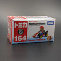 A boxed Dream TOMICA Mario Kart 8 Mario toy car package, shown on a dark gray surface. The box is white with red and blue sections, large white '164' text, and a printed image of Mario in a red and blue race kart.