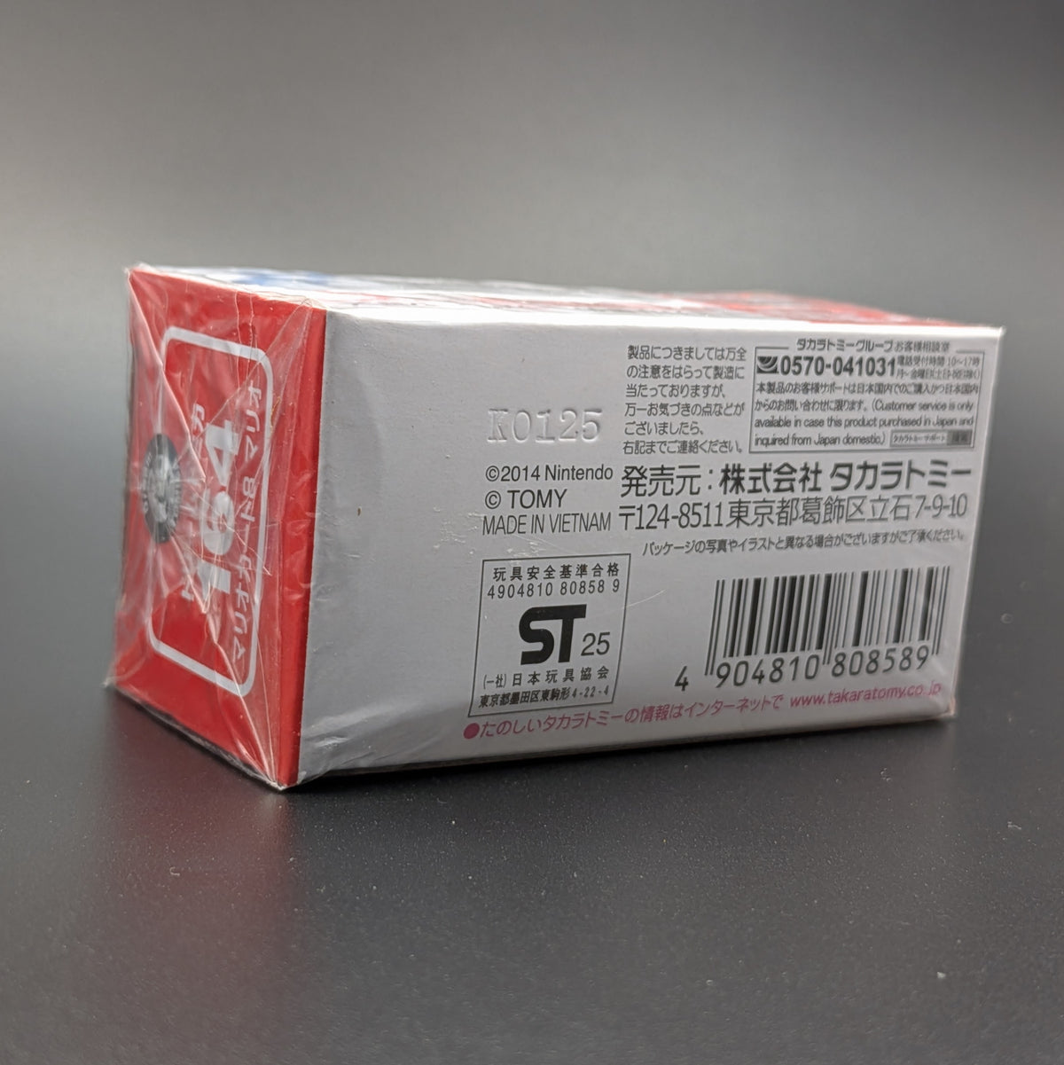 Nintendo Tomica box packaging, showing the back side with Japanese text, barcode, and product information on a dark gray surface.