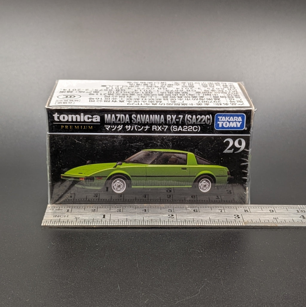 A boxed Tomica Premium Takara Toy Mazda Savanna RX-7 (SA22C) model car, shown in its original packaging with a clear plastic front and a ruler placed in front for scale on a dark gray background.