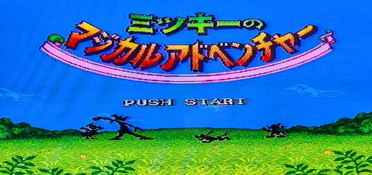 The Japanese video game title screen for 'Mickey's Magical Adventure' featuring stylised pixel art of a blue sky, green grass, and colourful title text with 'PUSH START' below. Released by Nintendo for the Super Famicom (SFC)