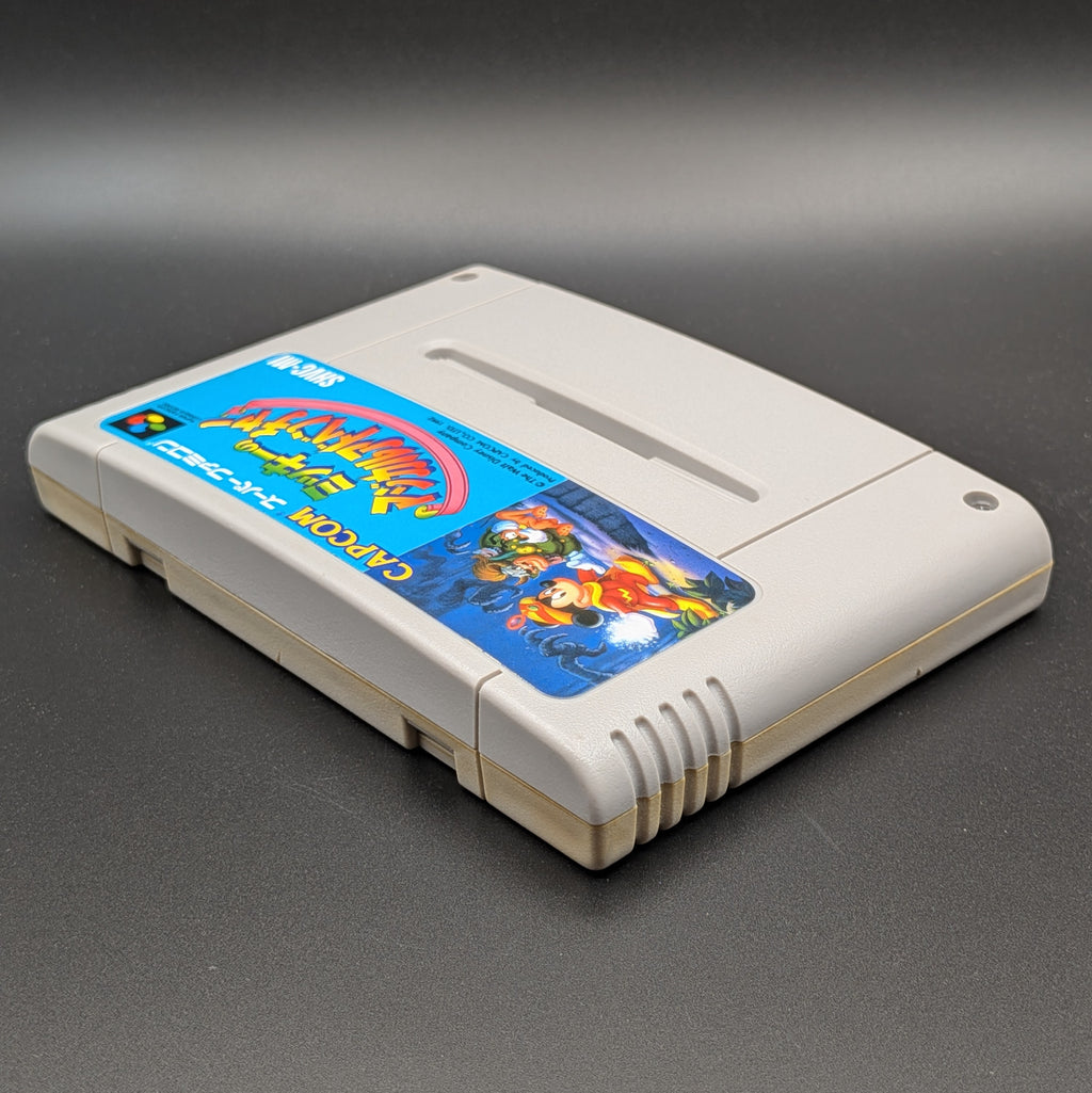 Mickey's Magical Adventure video game cartridge for Nintendo's Super Famicom (SFC) Entertainment System, shown laying on its back with the label facing upwards. Showing the left hand side and top edge. It is displayed on a dark grey background.