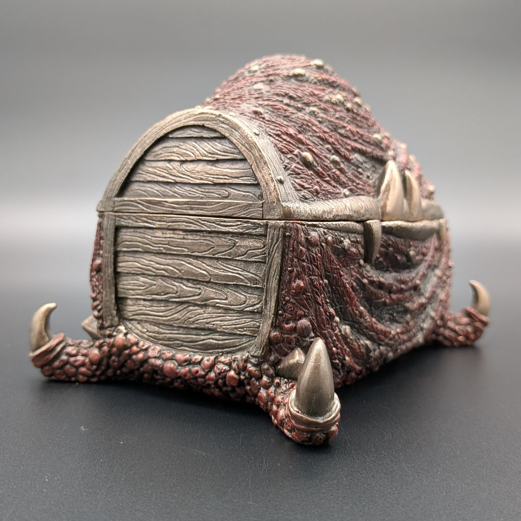 A fantasy miniature mimic chest, with textured reddish-brown skin and claws, photographed on a dark gray studio background.